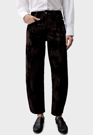 Persona che indossa pantaloni in velluto nero con gamba dritta e scarpe slip-on nere, abbinati a una camicia bianca a maniche lunghe.