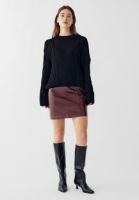 Črn pulover z pletenico, maroon usnjena mini krila in črne čevlje z visokimi petami do kolen. Gladke teksture in oprsani kroji so izraziti.