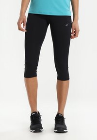 Czarne legginsy capri wykonane z elastycznego materiału, charakteryzujące się dopasowanym krojem i eleganckim wyglądem. W połączeniu z czarnymi butami sportowymi, co zwiększa mobilność.