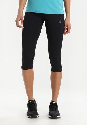 Leggings capri noirs en tissu extensible, offrant une coupe ajustée et un design élégant. Associés à des chaussures de sport noires, améliorant la mobilité.