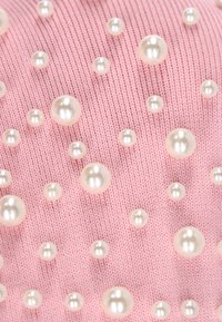 Tela rosa con una variedad de cuentas similares a perlas de diferentes tamaños, distribuidas uniformemente por toda la superficie, creando un patrón texturizado.