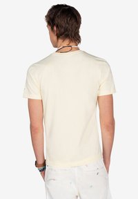 Camiseta de manga corta y cuello redondo en suave algodón amarillo pálido. Presenta una parte trasera lisa sin logotipos ni patrones visibles.