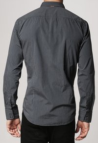 Donker gestreept shirt met lange mouwen en een aansluitend ontwerp, voorzien van dunne verticale lijnen en een afgeronde zoom. De achterkant vertoont een subtiel textuurdetail.