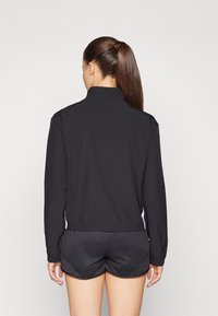 Sort atletisk jakke med høj krave og elastisk kant, parret med sorte shorts. Glat stof med hvide side accenter.