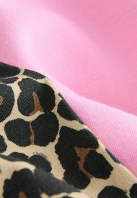 Tekstiler i pink og gyldent leopardmønster. Det pink stof har en blød tekstur; leopardmønsteret er på en glat, beige baggrund med sorte pletter.