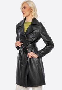 Cappotto lungo in pelle nera con un davanti doppiopetto, grande colletto e cintura. Presenta due tasche laterali e una texture liscia e lucida.