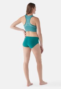Teal sportstopp med racerback-design och textilstruktur, kombinerad med teal-shorts och sedd bakifrån. Snygg, åtsittande passform.