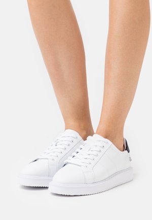 White leather sneakers with a rounded toe, flat sole, and textured detail on the heel. Features white laces and minimal branding.