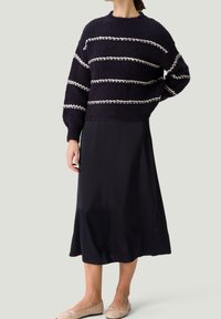 Pull en maille bleu marine avec rayures blanches, col rond et manches ballon, associé à une jupe en satin noire mi-longue et des ballerines beige.