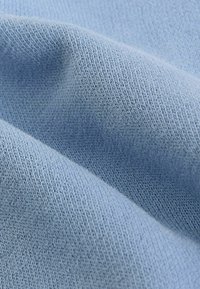 Detailný záber na mäkkú, svetlomodrú pleteninu s viditeľnou textúrou a jemnými záhybmi.