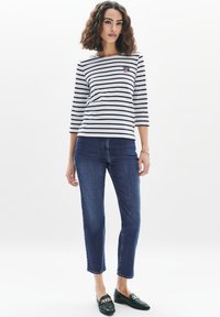 Randig båtneck-tröja i marinblått och vitt, ¾ ärmar, marinblå broderidetalj; matchad med mörkblå raka jeans och svarta loafers.