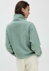 Hellgrüner Fleece-Pullover mit hohem Kragen, lockerer Passform, gerippten Bündchen und einer Rückennaht. Weicher, strukturiertes Material.