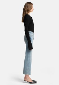 Top a maniche lunghe a coste nero abbinato a jeans a gamba dritta blu chiaro e décolleté neri a punta. L'outfit presenta un design fitted e linee pulite.