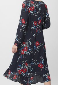 Klänning med blommönster i mörkblått, med lång ärm, volangkant, röda och blå blommor, samt en figurnära midja.