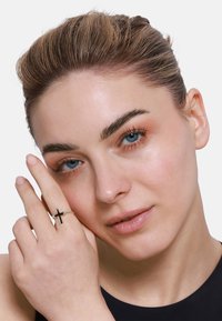 Srebrny pierścionek z czarnym wzorem krzyża. Modelka prezentuje pierścionek na palcu, ukazując gładką teksturę na tle neutralnego koloru skóry.