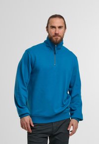 Niebieski polarowy pulower z wysokim kołnierzem i pół-zamkiem z przodu. Posiada długie rękawy oraz luźny krój z fakturowanym wykończeniem.