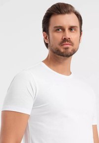 Weißes Baumwoll-T-Shirt mit Rundhalsausschnitt und kurzen Ärmeln, mit glatter Textur und tailliertem Design, präsentiert an einem Model.