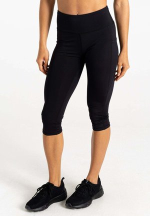 Schwarze Capri-Leggings mit hohem Bund, dehnbarem Material und seitlichen Taschen, kombiniert mit schwarzen Sportschuhen.