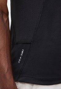 Κοντινό πλάνο μαύρου αθλητικού πουκαμίσου Dri-FIT που φοριέται στο άνω μέρος του κορμού, εμφανίζοντας διάτρητο πλευρικό πάνελ και ορατές ραφές.