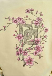 Sweatshirt jaune avec un graphisme central représentant un logo entrelacé avec des illustrations de fleurs roses et des branches, détaillé par un dessin au trait.