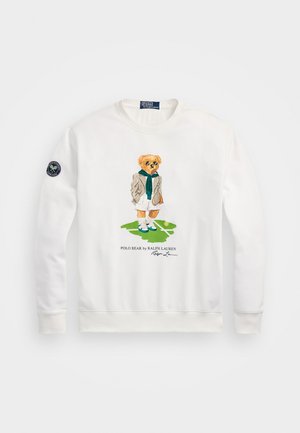 Bílá mikina s potiskem karikatury medvěda v bundě a šále, který drží tenisovou raketu. Obsahuje logo na rukávu.