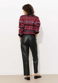 Pull en tricot avec un motif géométrique multicolore, associé à un pantalon en cuir noir et des ballerines noires avec des clous en argent, vu de derrière.