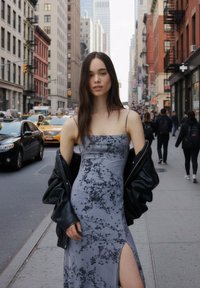 Grå blommig klänning med sidospalt, gjord av mjukt material. Lager-på-lager med en svart läderjacka. Urban gatubild i bakgrunden.