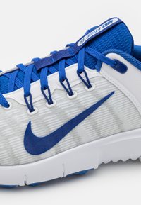 Sneakers Nike Free 5.0 w szaro-białej cholewce, niebieskimi akcentami, teksturowanym materiałem oraz kontrastującymi niebieskimi sznurówkami, z charakterystycznym logo Swoosh.