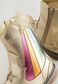 Botines metálicos dorados con acentos de estrellas y rayas coloridas en rosa, púrpura, verde y naranja; textura suave; cierre con cremallera lateral.