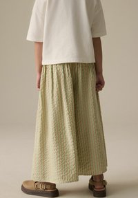 Jupe maxi rayée vert clair avec des plis, faite d'un tissu texturé. Associée à des sandales à boucle marron et à une chemise blanche à manches courtes.