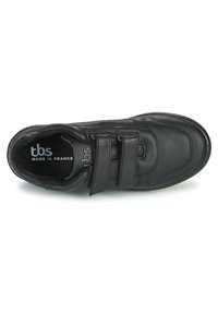 Chaussure en cuir noir avec bandoulières en Velcro, bout arrondi, surface texturée et col rembourré. Marque visible à l'intérieur de la chaussure.