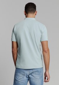 Lichtblauw polo shirt met een zachte textuur, korte mouwen en een kraag. G gedragen met denim jeans, wat een eenvoudig ontwerp laat zien. Achteraanzicht.