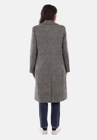 Cappotto grigio con motivo a spina di pesce, taglio lungo, colletto a revers e polsini con bottoni, abbinato a jeans blu e sneakers bianche.