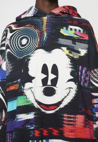 Sudadera con capucha que presenta un gran gráfico de Mickey Mouse en blanco y negro, sobre un fondo abstracto multicolor con patrones digitales.