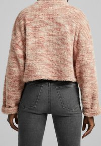 Różowy, przycięty, miękki sweter w kremowe paski, z długimi rękawami i miękką teksturą, zestawiony z ciemnoszarymi dżinsami.