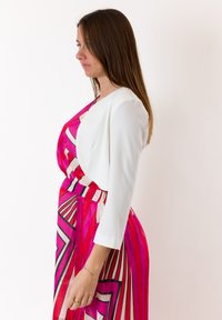 Giacca bianca a tre quarti sovrapposta a un vestito rosa con motivo geometrico a righe. Tessuto liscio con una silhouette fluida.