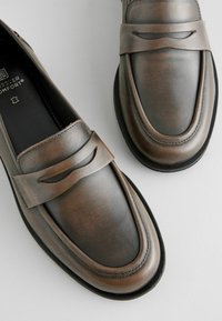 Loaferi din piele maronie cu o finisare netedă, design subțire și detalii decorative cu decupaj pe curea. Tacâm de cauciuc ușor.