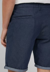 Navy Denim-Shorts mit aufgerollten Säumen, Rückentaschen und einer glatten Textur. Der Bund verfügt über Gürtelschlaufen für eine verstellbare Passform.