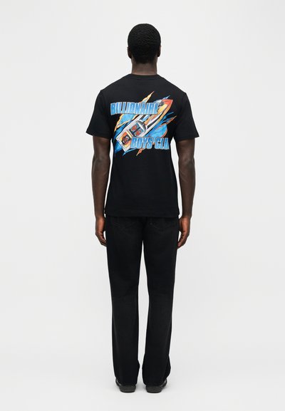 Άνδρας που φοράει μαύρο μπλουζάκι με πολύχρωμο πύραυλο και το κείμενο "Billionaire Boys Club" στην πλάτη, συνδυασμένο με μαύρο παντελόνι, στεκόμενος με το πρόσωπο προς τα πίσω.