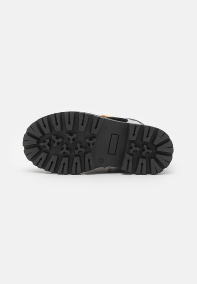 Chaussures à semelle en caoutchouc avec un motif de semelle profond, dotées d'une base noire robuste et d'accents jaunes sur le dessus. Surface texturée pour une meilleure adhérence.