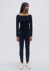 Μπλε ναυτικού μακρυμάνικο τοπ με ντεκολτέ έξω από τους ώμους, σε συνδυασμό με στενές μπλε ναυτικού παντελόνες με πλαϊνές τσέπες και χρυσές λεπτομέρειες. Λευκά αθλητικά παπούτσια.