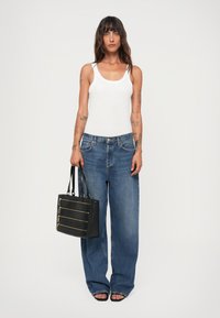 Weißes Rippentop, blaue weit geschnittene Jeans, schwarze Handtasche mit goldenen Reißverschlüssen und Logo sowie schwarze Sandalen mit offenen Zehen.