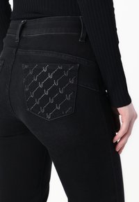 Svarte denimjeans med høy midje og en dekorativ baklomme med et symmetrisk mønster i sølvpynt.