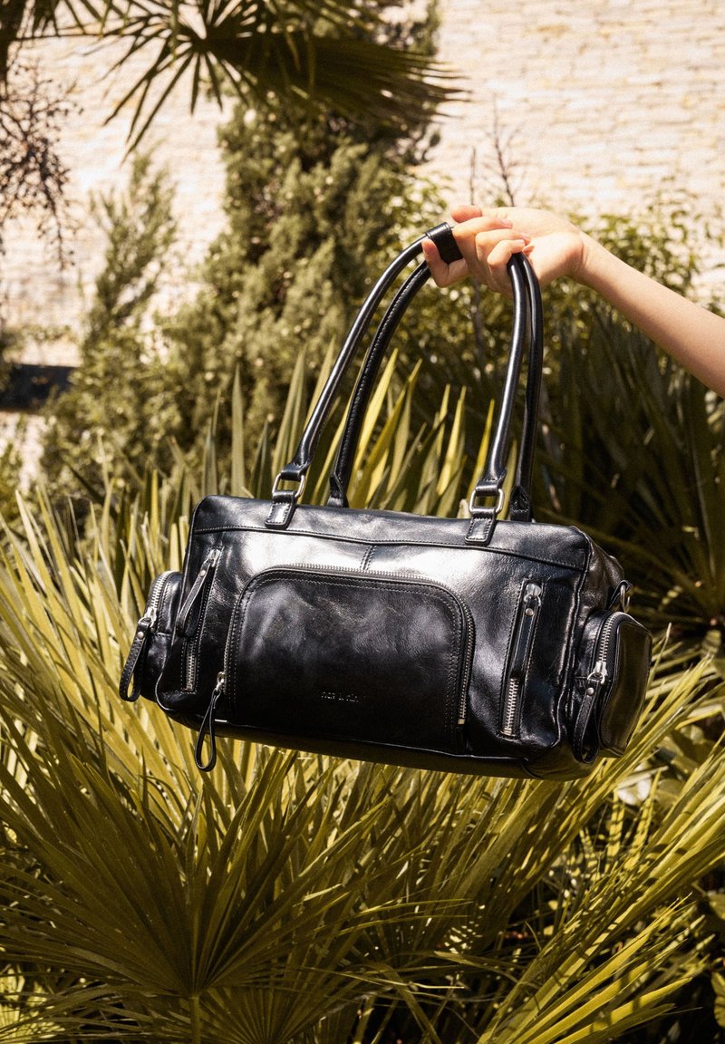 Black leather handbag with dual top handles, multiple zippered pockets, smooth texture, rectangular shape, and glossy finish.