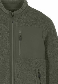 Veste en polaire vert olive avec un corps texturé et duveteux et un panneau d'épaule lisse. Comprend une poche poitrine zippée et des poches latérales.