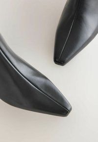 Scarpe nere in pelle con punta affusolata, caratterizzate da una superficie liscia e dettagli di cucitura minimi, viste dall'alto, che evidenziano il loro design elegante.