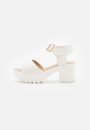 Witte platform sandalen met een open teen, verstelbare enkelband en een gestructureerde zool. Heeft een dikke hak en een minimalistisch ontwerp.