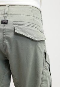 Cargo byxor i ljusgrön tyg med rak passform, flera fickor och en G-Star logotel på baksidan. Texturerade ytdetaljer är synliga.