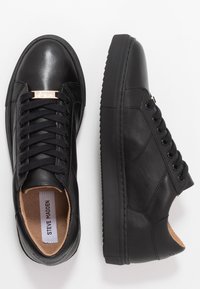 Czarne skórzane sneakersy niskie z czarnymi sznurowadłami i złotą metką, pokazujące widok z góry lewej buta oraz widok z boku prawego buta.
