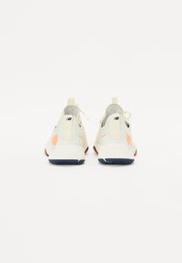Light beige athletic shoes with an orange accent, textured rubber sole, and cushioned heel. Features a pull tab and laces for secure fit.